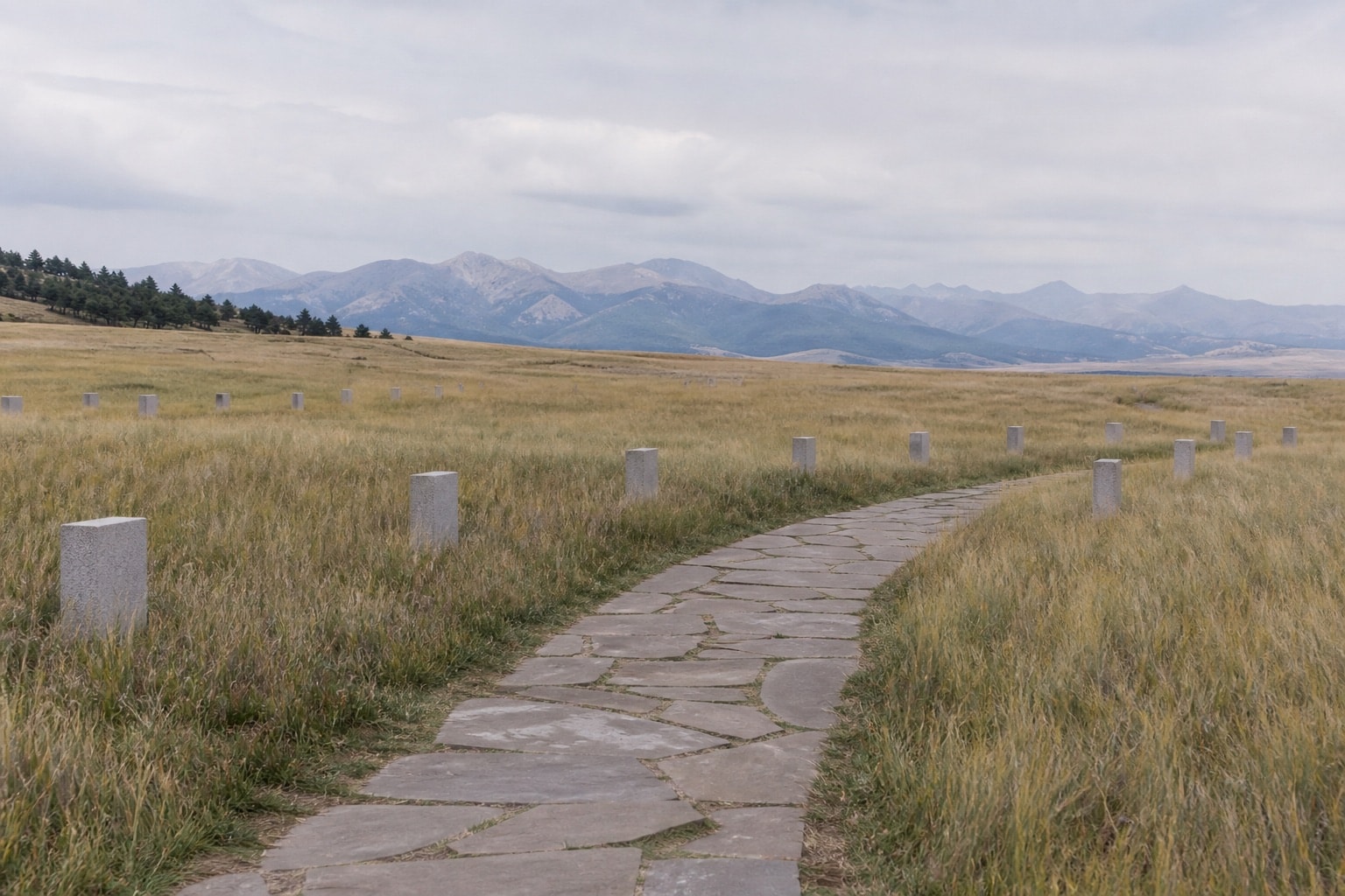 A quiet unlabelled memorial landscape on open grassland beneath distant mountains
