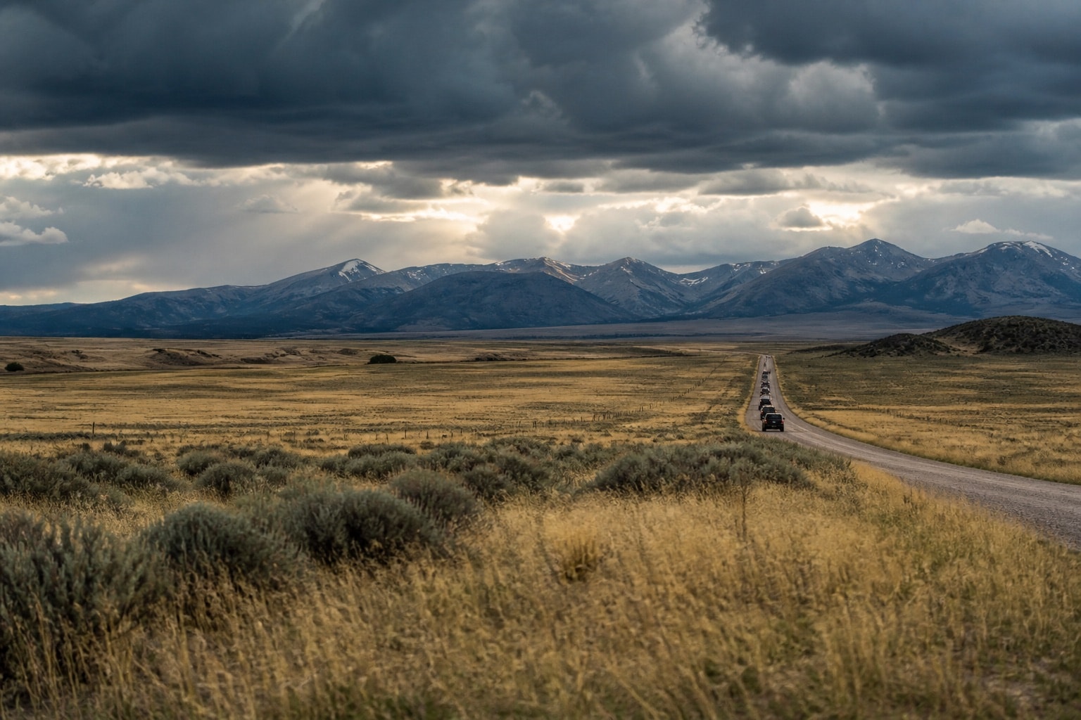 Unmarked utility vehicles crossing a wide Montana grassland beneath a changing sky